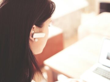 woman wearing earpiece using white laptop computer