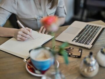 person writing on a notebook beside macbook