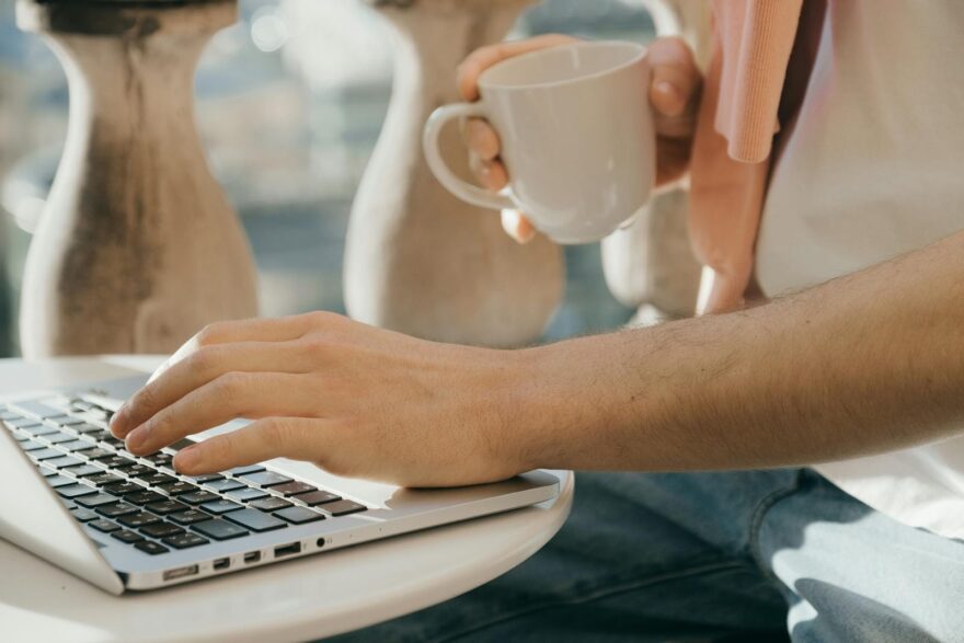 Close-up of a person working outdoors with a laptop and coffee in hand.
