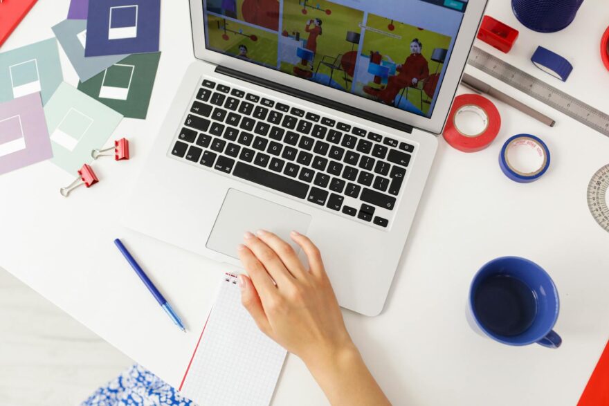 A creative workspace featuring a laptop, design tools, and a hand writing on a notepad.